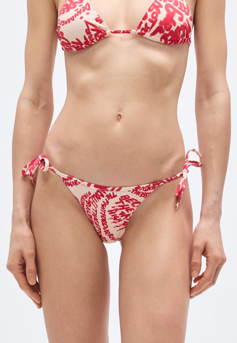 Punane ja beež bikiin, millel on kolmnurkse lõikega ülaosa ja külgedelt seotavad püksikud, katmist pakub julge graafiline trükk kangal.