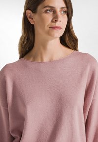 Jasnoróżowy sweter z szerokim, okrągłym dekoltem, długimi rękawami i miękkim, teksturowanym materiałem. Charakteryzuje się luźnym krojem i minimalnymi detalami szwów.