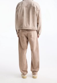 Beige denimjakke og matchende bukser. Begge har en afslappet pasform med elastiske manchetter. Struktureret stof med minimal syning og lomme detaljer.
