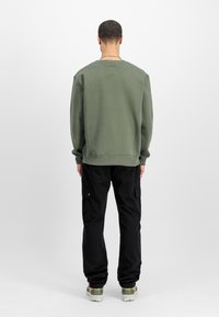 Sudadera verde oliva con cuello redondo, dobladillo y puños acanalados, combinada con pantalones cargo negros con bolsillos laterales.