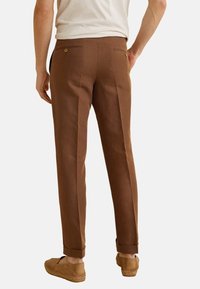 I pantaloni in lino marrone presentano una vestibilità su misura, due tasche posteriori con bottoni e orli risvolti. Il tessuto ha una consistenza liscia.