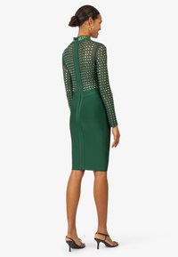 Abito midi verde con top trasparente a maniche lunghe impreziosito da motivi quadrati. Silhouette aderente e chiusura con zip sul retro.