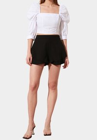 Bílý krátký top s nafouklými rukávy a čtvercovým výstřihem, doplněný černými rozšířenými šortkami. Celý vzhled doplňují průhledné sandály na podpatku.