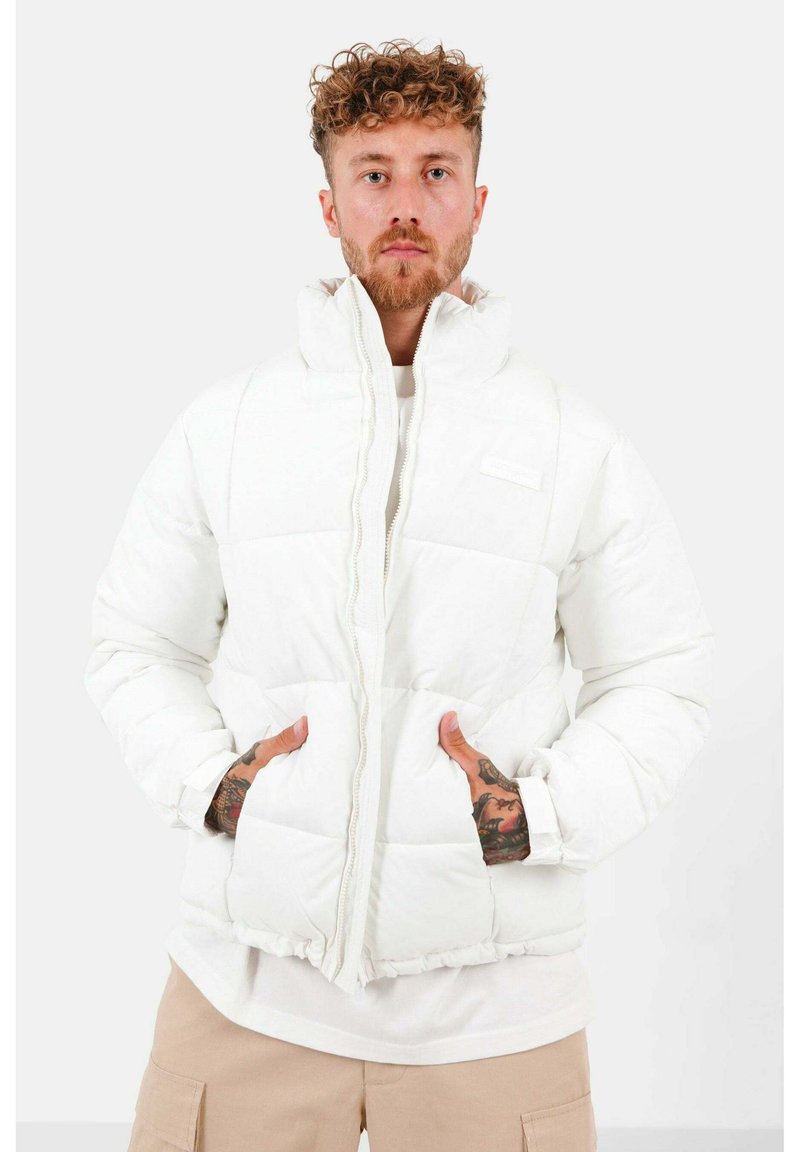 Veste matelassée blanche avec col montant, fermeture éclair et deux poches devant ; présente une texture matelassée et un ourlet ajusté.