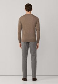 Bruine langslavige trui van fijn gebreide stof, gecombineerd met lichtgrijze broek en donkerbruine schoenen. Eenvoudig en slim design.