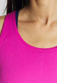 T-shirt atlético ajustado de tejido rosa brillante con una textura suave y un escote redondeado, superpuesto sobre una camiseta azul debajo.