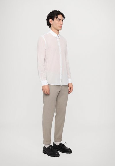 Camisa blanca de manga larga y botones, de tela ligera y suave, combinada con pantalones beige y zapatos negros de cordones.