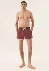 Bordowe kąpielówki z białym sznurkiem w pasie, bocznymi kieszeniami oraz kontrastowym białym wykończeniem. Wykonane z lekkiego materiału.