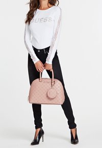 Biała bluzka z długim rękawem z cekinowym logo „GUESS”, koronkowe akcenty. Czarne dopasowane dżinsy. Jasnoróżowa, usztywniana torebka z wytłoczonym logo i okrągłą zawieszką.