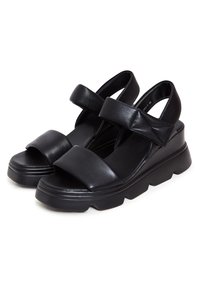 Paire de sandales épaisses noires avec de larges brides et des semelles épaisses, conçues pour un usage décontracté et le confort.