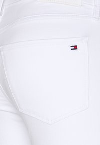 Primer plano de unos jeans de mezclilla blanca que muestran el bolsillo trasero con el pequeño logotipo de bandera de Tommy Hilfiger bordado en la esquina superior derecha.