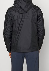 Černá lehká bunda s kapucí, která má hladký, lesklý povrch, elastické manžety a rovný lem. Jednoduchý design bez viditelných log.