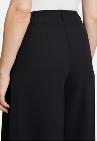 Zwarte wijde broek met een op maat gemaakte taille, voorzien van riemlussen en een gladde textuur. De tailleband is net afgewerkt zonder zichtbare sluitingen.