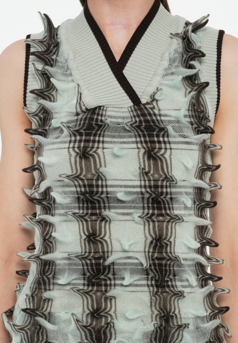 Top senza maniche lavorato a maglia in verde menta chiaro con un motivo marrone. Presenta volant asimmetrici lungo i bordi per una texture e un interesse visivo.