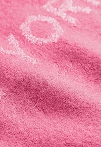 Materiał polarowy w intensywnym różowym kolorze, z haftowanymi detalami w jaśniejszym odcieniu, o miękkiej i fakturowanej powierzchni.