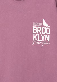 Fialové bavlnené tričko s bielou grafickou potlačou, ktorá obsahuje "11202", "BROOKLYN", ilustráciu holuba a "New York".
