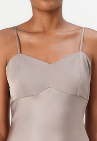 Camisola in seta con scollatura a V, spalline sottili e un tessuto taupe liscio con una leggera lucentezza e cuciture sartoriali.