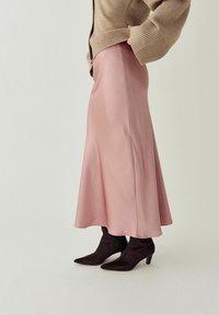 Kvinde iført en beige trøje med vide ærmer, en flydende pink satin midi nederdel og sorte ankelstøvler med spids tå og hæl.