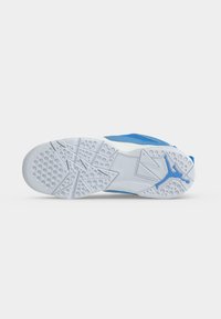 Σόλα ενός μπλε και λευκού αθλητικού παπουτσιού με υφή λαβής και μπλε λογότυπο Jumpman κοντά στη φτέρνα σε ανοιχτό φόντο.