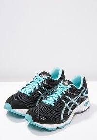 Scarpe da corsa nere con tomaia in rete e accenti turchesi. Le caratteristiche includono una suola ammortizzata, lacci a contrasto e un design elegante.