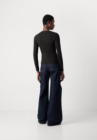 Black long-sleeve top made of ribbed fabric paired with dark blue, wide-leg jeans featuring contrast stitching. Simple design and texture.