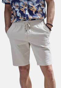 Light beige shorts featuring an elastic waistband with drawstring, side pockets, and a smooth fabric texture. Suitable for casual wear.