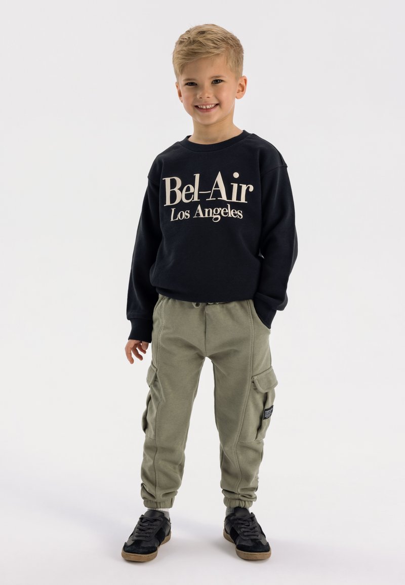 Zwarte sweatshirt met de tekst "Bel-Air Los Angeles", grijs-groene cargobroek en zwarte schoenen met tan kleurige zolen; casual kinderkleding.