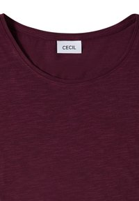 T-shirt bordeaux à col rond avec une étiquette blanche indiquant le nom de la marque "CECIL" cousue à l'intérieur du col.