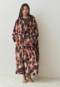 Oversized gewatteerde badjas van pluche stof met een bruin en zwart luipaardpatroon, voorzien van een ritssluiting en twee voorzakken.