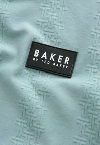 Gai zils audums ar faktūru. Melna taisnstūra birka ar tekstu "BAKER BY TED BAKER" ir izceltā.