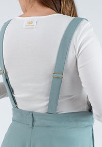 Licht teal verstelbare bretels met gouden hardware bevestigd aan een aansluitend wit geribbeld langemouwtop. Gladde stoftextuur, minimalistisch ontwerp.