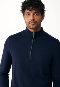 Marineblauwe gebreide trui met hoge kraag en kwart rits. Lichtgewicht stof met een gladde textuur en een aansluitend ontwerp.