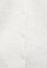 Hvit strikket cardigan med en myk tekstur, med fem runde knapper nedover midten og et ribbestrikket mønster gjennom hele.