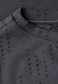 Tissu tricoté noir avec de petites découpes, présentant un décolleté arrondi et des bords côtelés, créant un design texturé et respirant.