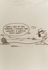 Jasno beżowa tkanina przedstawia rysunkowy wzór z psem trzymającym patyk oraz tekst w dymku o waflach i urządzeniu do ich robienia w tle.