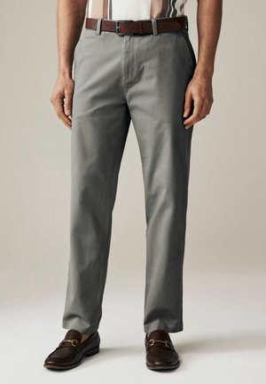 Pantalones grises de mezcla de algodón, con un corte recto, bolsillos frontales y un cinturón de cuero marrón. Combinados con mocasines oscuros.