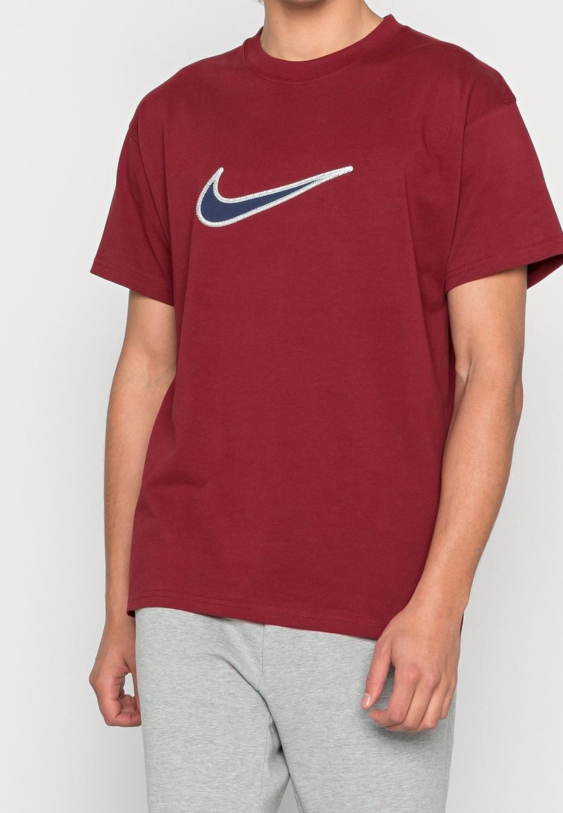 Maroon cotton T-shirt with a crew neckline and short sleeves, featuring a white and navy embroidered Nike swoosh logo on the chest.