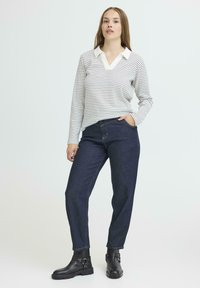 Gestreepte lange mouw top in crème en zwart met een kraag, gecombineerd met donkerblauwe high-waisted jeans en zwarte enkellaarsjes.