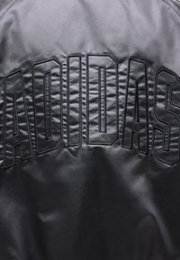 Sort skinnjakke med store broderte bokstaver "ADIDAS" på ryggen i en fet, omrisset font.