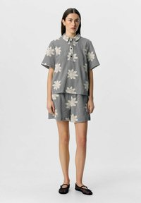 Ensemble de chemise à manches courtes à carreaux et de shorts, avec des motifs floraux blancs. Fabriqué en tissu léger, avec un col et des boutons.