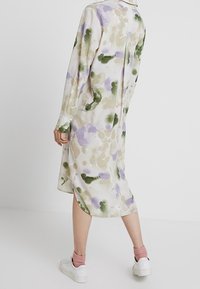 Lång knapplång klänning i lätt tyg, med ett akvarellmönster i lavendel, grönt och beige toner. Vita sneakers fulländar looken.