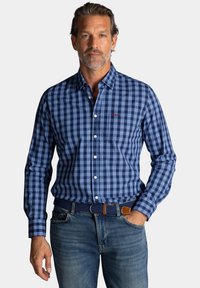 Blauwe gestructureerde blouse met lange mouwen, met verschillende tinten blauw en wit, gecombineerd met een bruine en blauwe gevlochten riem.