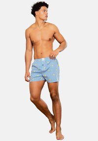 Blaue gestreifte Badeshorts mit gelben Entenmuster, elastischem Bund und lockerer Passform. Aus leichtem Material gefertigt.