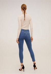Top de manga larga de color beige claro con canalé, combinado con jeans ajustados azules. Corte alto con bolsillos traseros y tacones negros con correa en el tobillo.