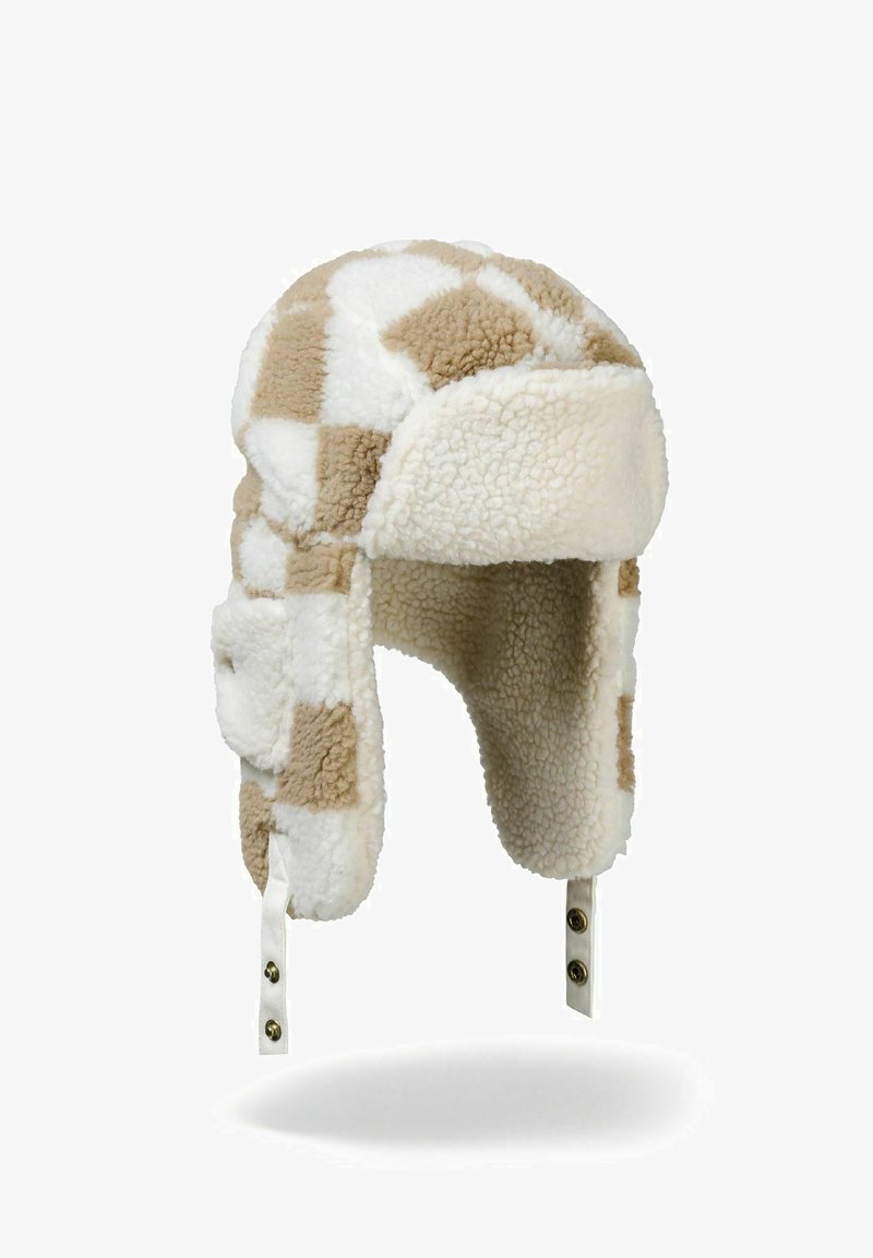 Chapeau trapper en fausse fourrure à carreaux marron et crème avec des rabats d'oreilles et des sangles réglables, présentant des accessoires de couleur or. Texture douce sur l'ensemble.