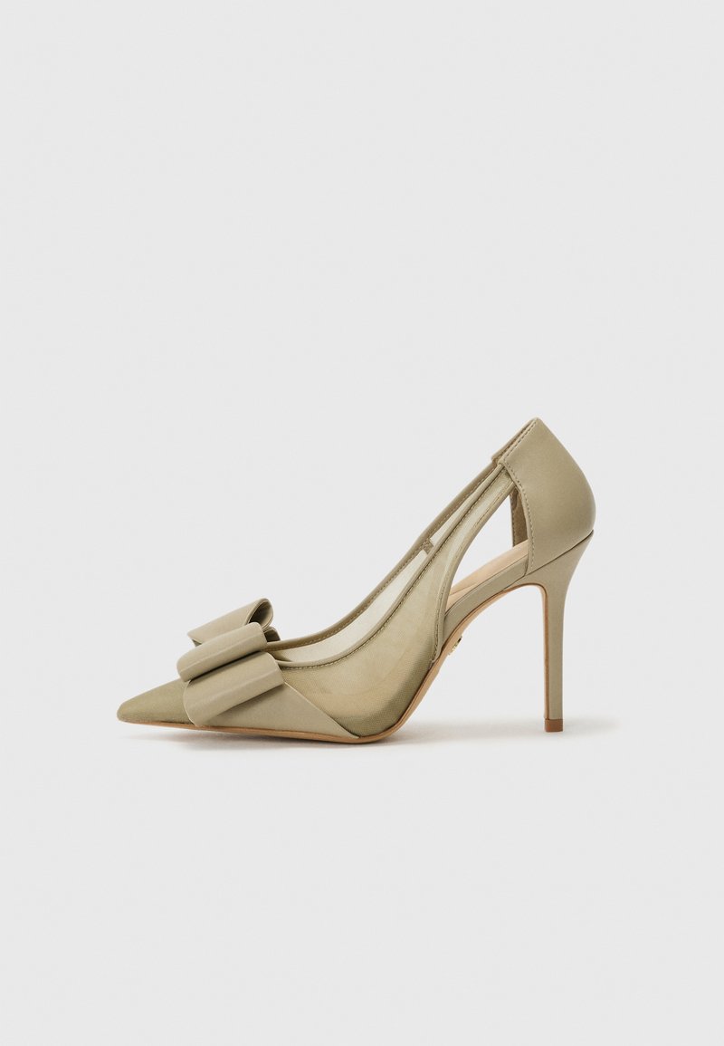 Beige høyhælte pumps med spiss tå, prydet med bue og utskårne sider. Glatt tekstur med blank finish og slank stiletthæl.