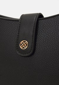 Czarna torebka ze skóry z teksturą, z okrągłym złotym elementem ozdobnym oraz zamknięciem na klapę. Gładkie przeszycia wzdłuż krawędzi.