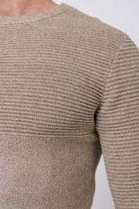 Pull en maille beige avec texture côtelée sur la partie supérieure, moitié inférieure lisse et col rond. Les détails texturés créent un effet superposé.