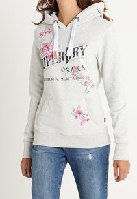 Sudadera gris claro con bordado floral en rosa y verde, bolsillo canguro delantero, capucha con cordones y puños y dobladillo acanalados.
