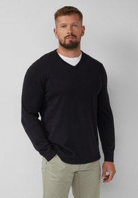 Schwarzer V-Ausschnitt-Pullover aus weichem Strickmaterial mit langen Ärmeln, kombiniert mit hellen Hosen. Verfügt über ein nahtloses Design und eine körperbetonte Silhouette.